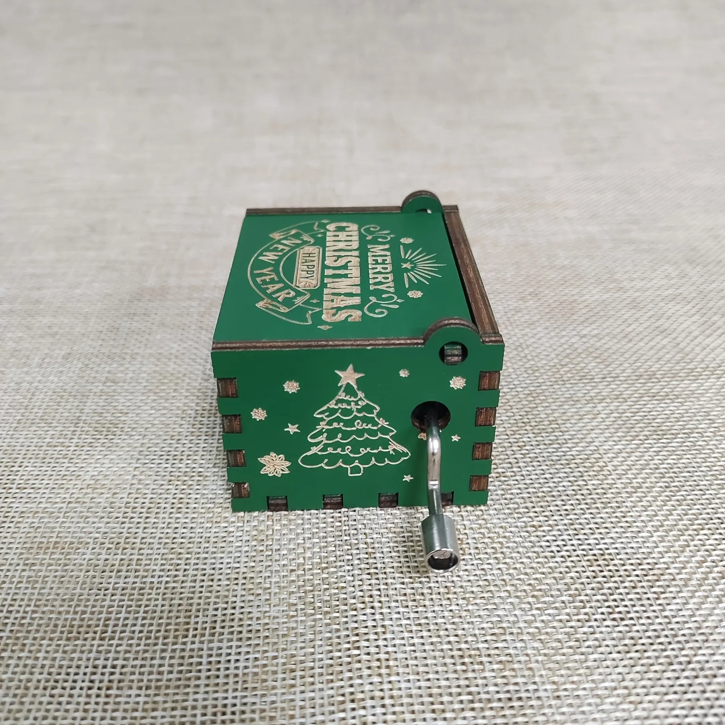 Green Christmas-themed hand crank music box on a textured fabric background
