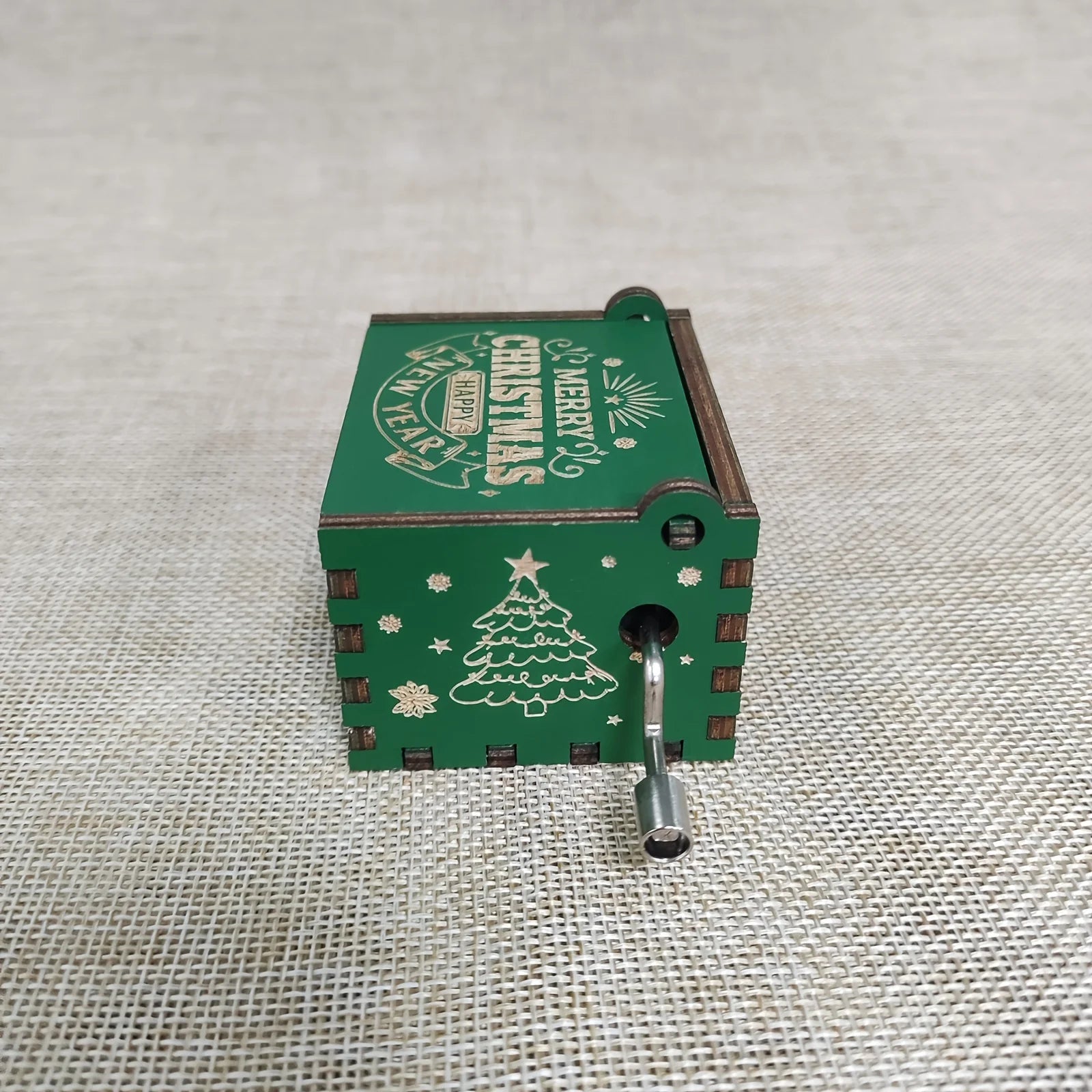 Green Christmas-themed hand crank music box on a textured fabric background