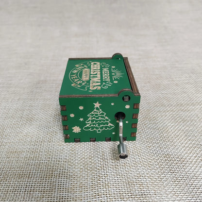 Green Christmas-themed hand crank music box on a textured fabric background