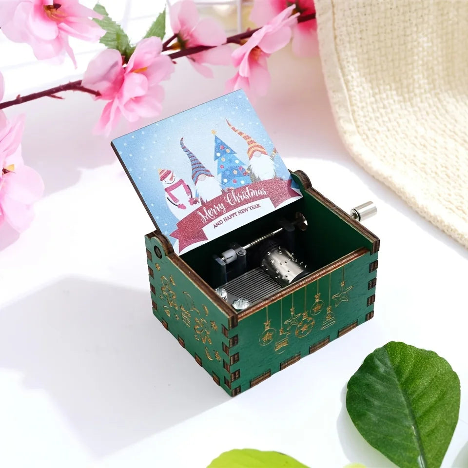 Green music box with a Christmas design on top, surrounded by pink flowers and a straw hat.