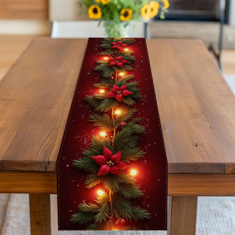 Red Christmas table runner with poinsettia flowers, evergreen branches and glowing light effect on a wooden table.